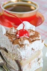 A cup of tea and a piece of cream cake with cherry