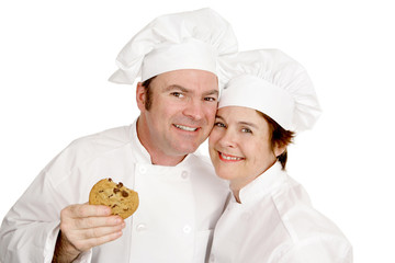 Couple of chefs smiling and enjoying a cookie.