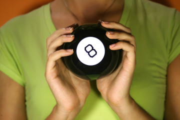 Woman holding in her hands magic 8 ball. Orange background.