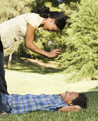 Woman standing over smiling man in grass taking his picture.