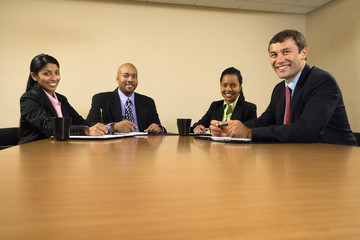Businesspeople sitting at conference table smiling.