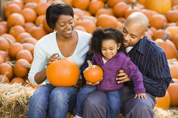 Happy family sitting on hay bales and holding pumpkins. - Powered by Adobe