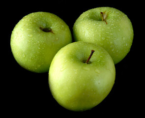 Three fresh green apples with water drops isolated on black