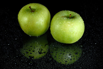 Two fresh green apples with water drops on wet black surface