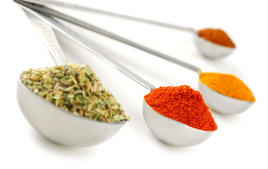Assorted spices in metal measuring spoons on white background