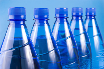 five blue water plastic bottles aligned, focus on the first one