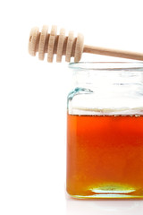 Honey jar and wooden drizzler, reflected on white background