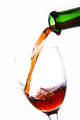 Pouring the red wine into the wineglass in white background.