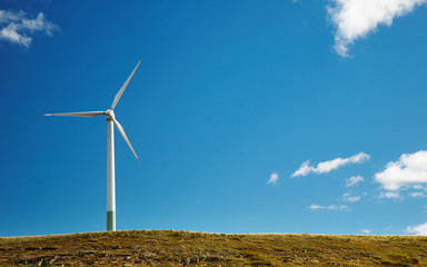 Wind turbine on top of hill against blue sky background