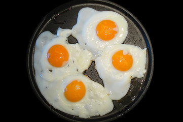 Four fried eggs in a frying pan isolated on black