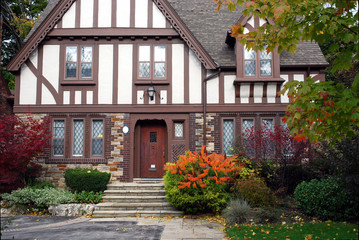 tudor style home with brown trim and sumac bush in fall - obrazy, fototapety, plakaty