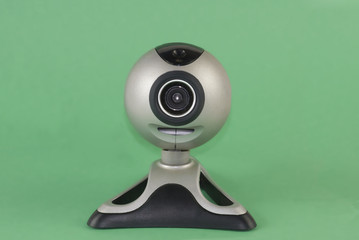A silver webcam set against a green background