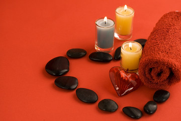 red towel, candles, river stones and red heart on red background