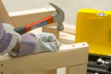 man with safety gloves holding screw and hammer