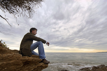 jeune homme assis seul face à la mer solitude tristesse - obrazy, fototapety, plakaty