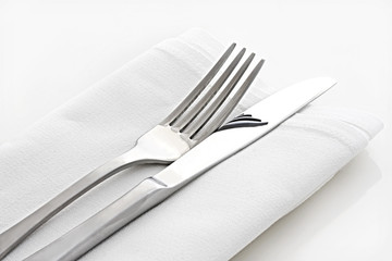 Silver knife and fork on white linen napkin.