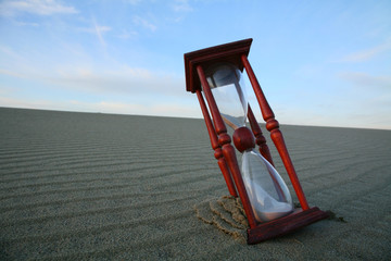 Hourglass on the evening dune and wavy lines of sand.