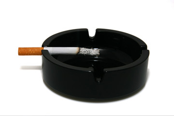 A smoking cigarette with the filter in a black ashtray.