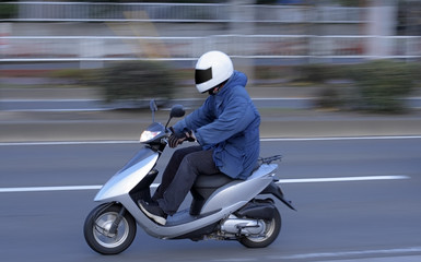 Panning image of a man riding a scooter in a city.