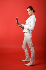 A young woman typing on a laptop computer isolated on red