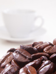 Close up of coffee beans with a cup in background.