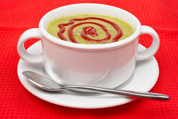 Spinach puree on white cup with spoon over red mat. Shallow DOF