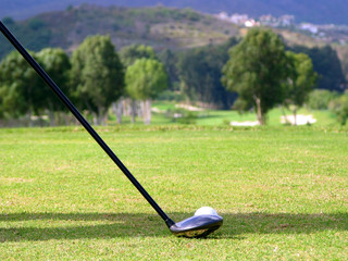 Golf club and ball on the tee with the fairway in the distance.