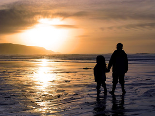 Two children holding hands whilst watching a beach sunset.