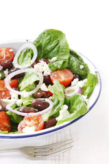 Greek salad in enamel bowl on rustic white timber table