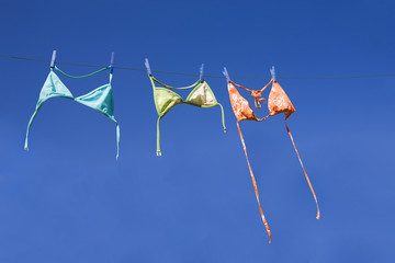 Three colorful bikini tops drying on washing line
