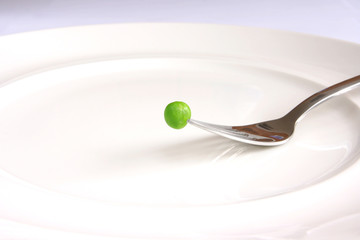 Single fresh green pea above white plate on fork