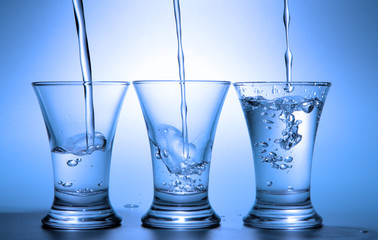 Clear liquid pour into three wineglasses toned in blue color