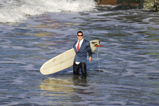 homme en smoking avec une planche de surf les pieds dans l'eau