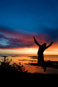 A person jumping by the ocean at sundown