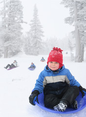Four year old boy sledding in snowy landscape