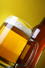 Beer with froth and bottle close-up over yellow background