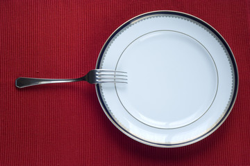 fork and porcelain plate over red (copy space in the plate)