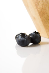 blueberries near a wooden bowl , isolated over white background