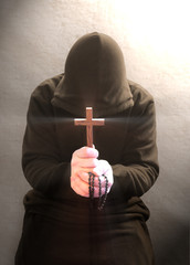 A monk praying with a rosary and crucifix in his hand.