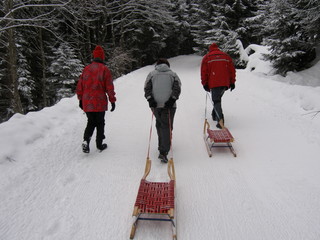 Drei menschen auf rodelweg in verschneiter winterlandschaft 
