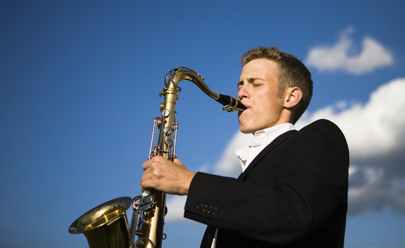 Young saxophone player playing his instrument outdoors.