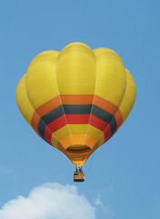 Yellow hot-air balloon flying mid-air. Blue sky background.