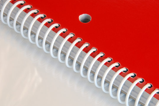 Close up of red spiral notebook on reflective surface.
