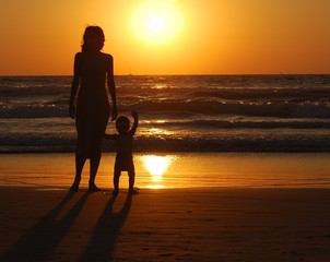young woman with small child on the sea shore on sunset