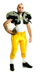 An American football player. Standing, holding helmet.