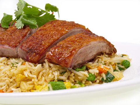 ein Teller mit knusprig gebratener Ente auf gebratenem Reis mit Gemüse, freigestellt auf weißem Hintergrund