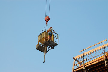 Fototapeta na wymiar Builder transported by crane with concrete hopper