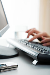 Human hands on the keyboard with the cell lying near by