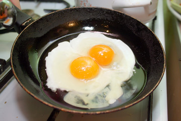 Two fried eggs in hot pan on gas stove