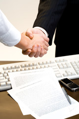 View of handshake over paper, keyboard, pen, cell at the back